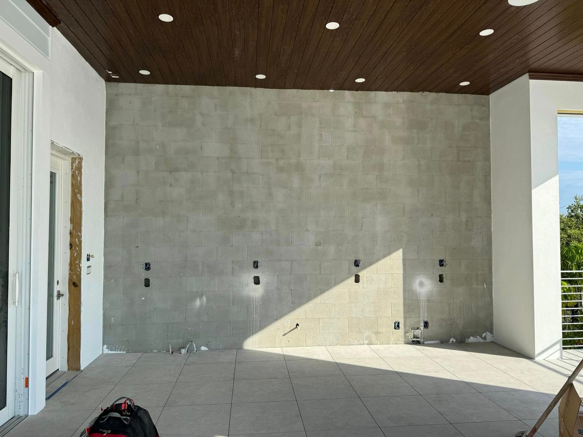 Exterior patio with light grey tile walls and flooring, dark wood ceiling, and electrical outlets.