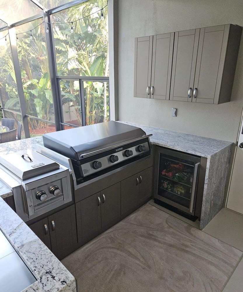 Outdoor kitchen with stainless steel grill, cabinets, countertop, and a mini-fridge.