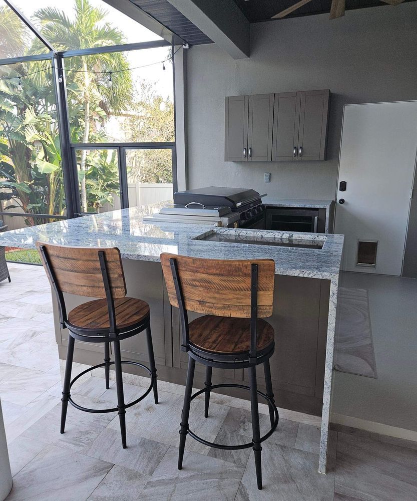Outdoor kitchen with granite countertop and two wood and metal bar stools. Gray cabinetry and built-in grill.