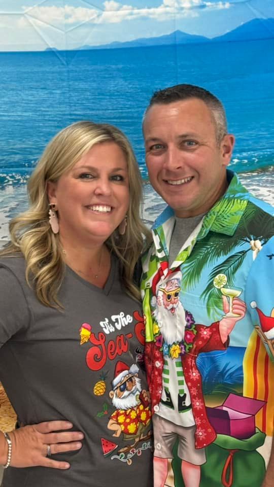 Woman and man smiling, posing in front of beach backdrop; wearing Christmas-themed apparel.