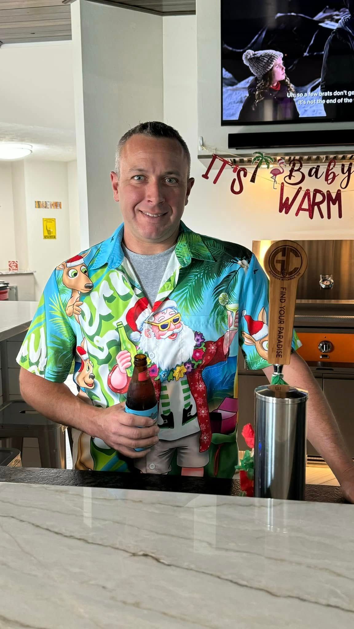 Man in Christmas shirt holding beer behind a bar. 