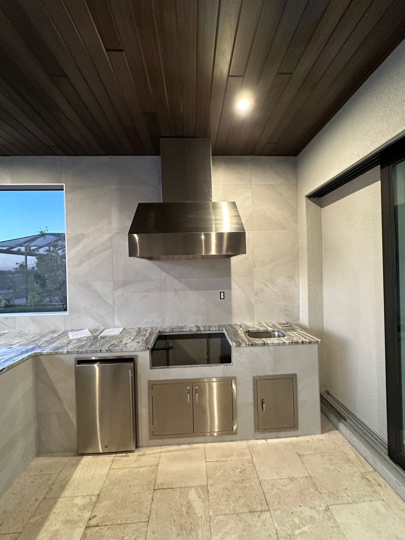 Outdoor kitchen with stainless steel appliances, marble tile, and wood ceiling.