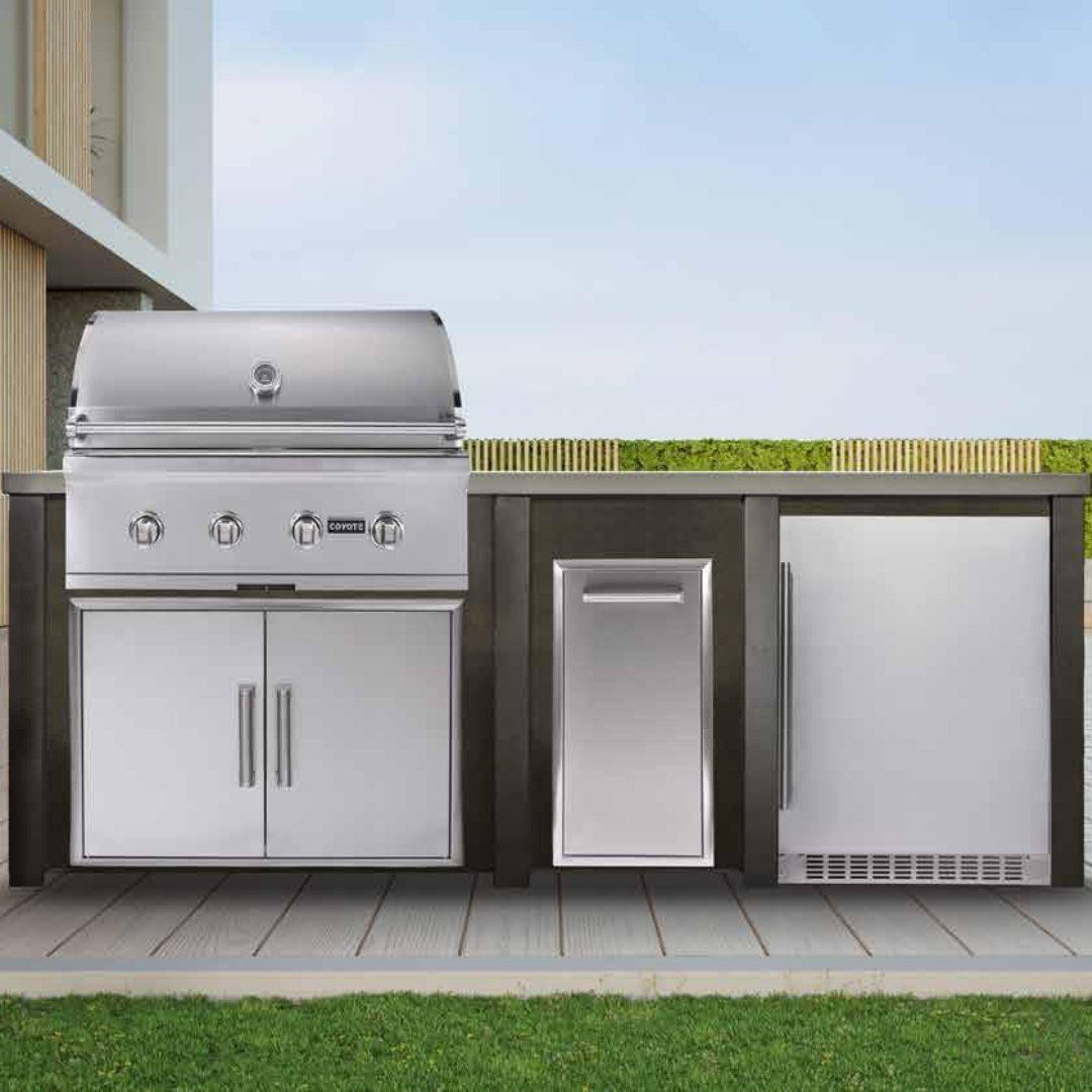 Outdoor kitchen with stainless steel grill, trash compactor, and refrigerator on a deck.