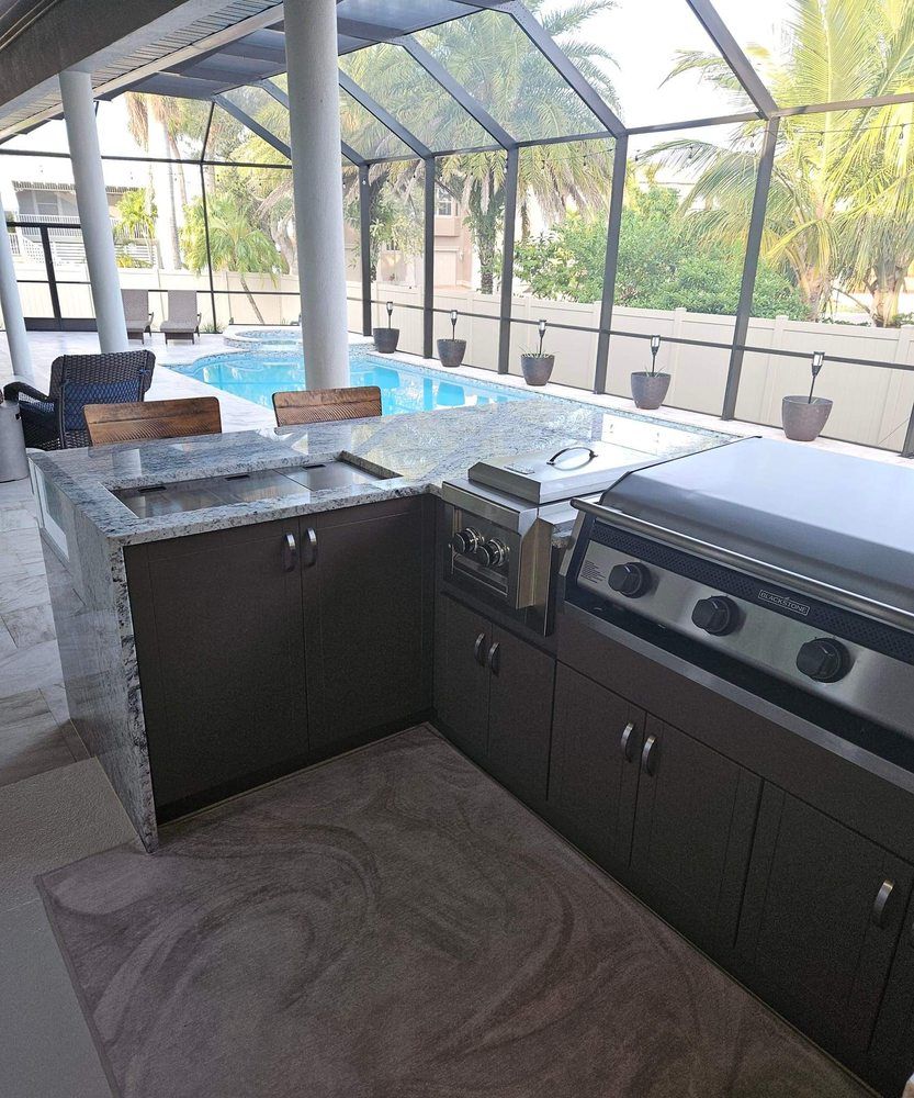 Outdoor kitchen with granite countertop and built-in grill, near a pool.