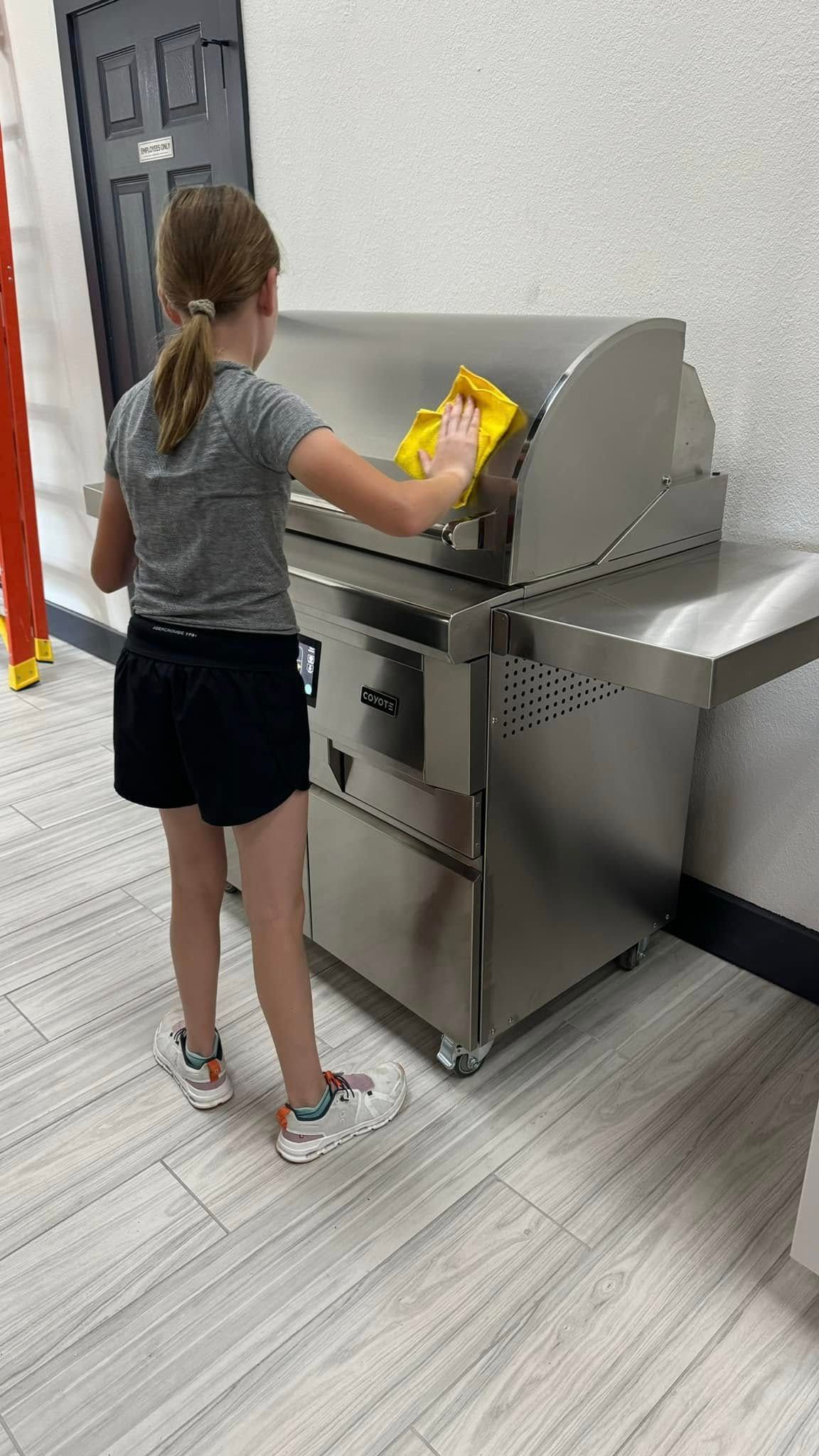 A person cleans a stainless steel grill with a yellow cloth.