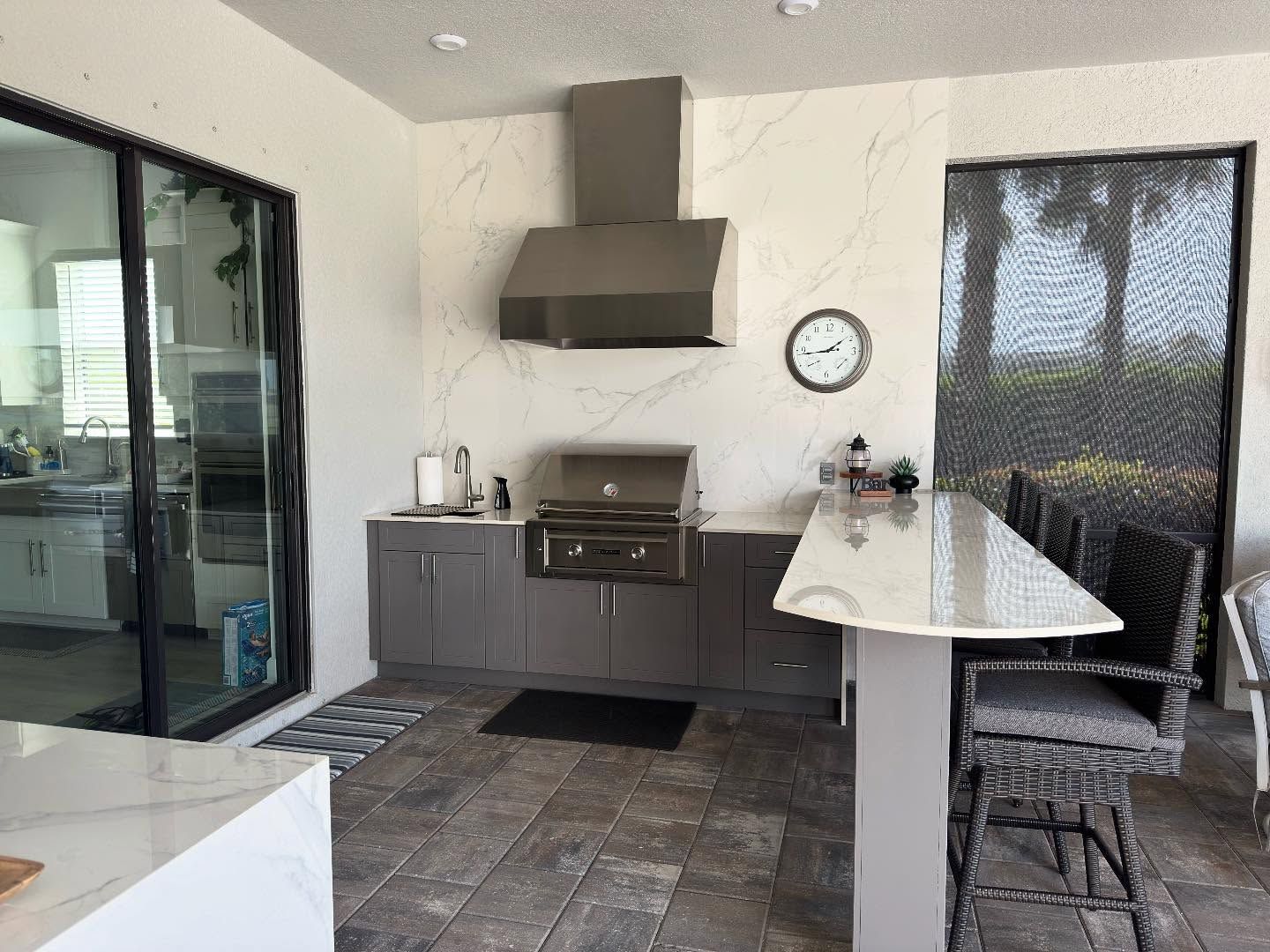 Outdoor kitchen with a stainless steel grill, cabinets, and bar seating.