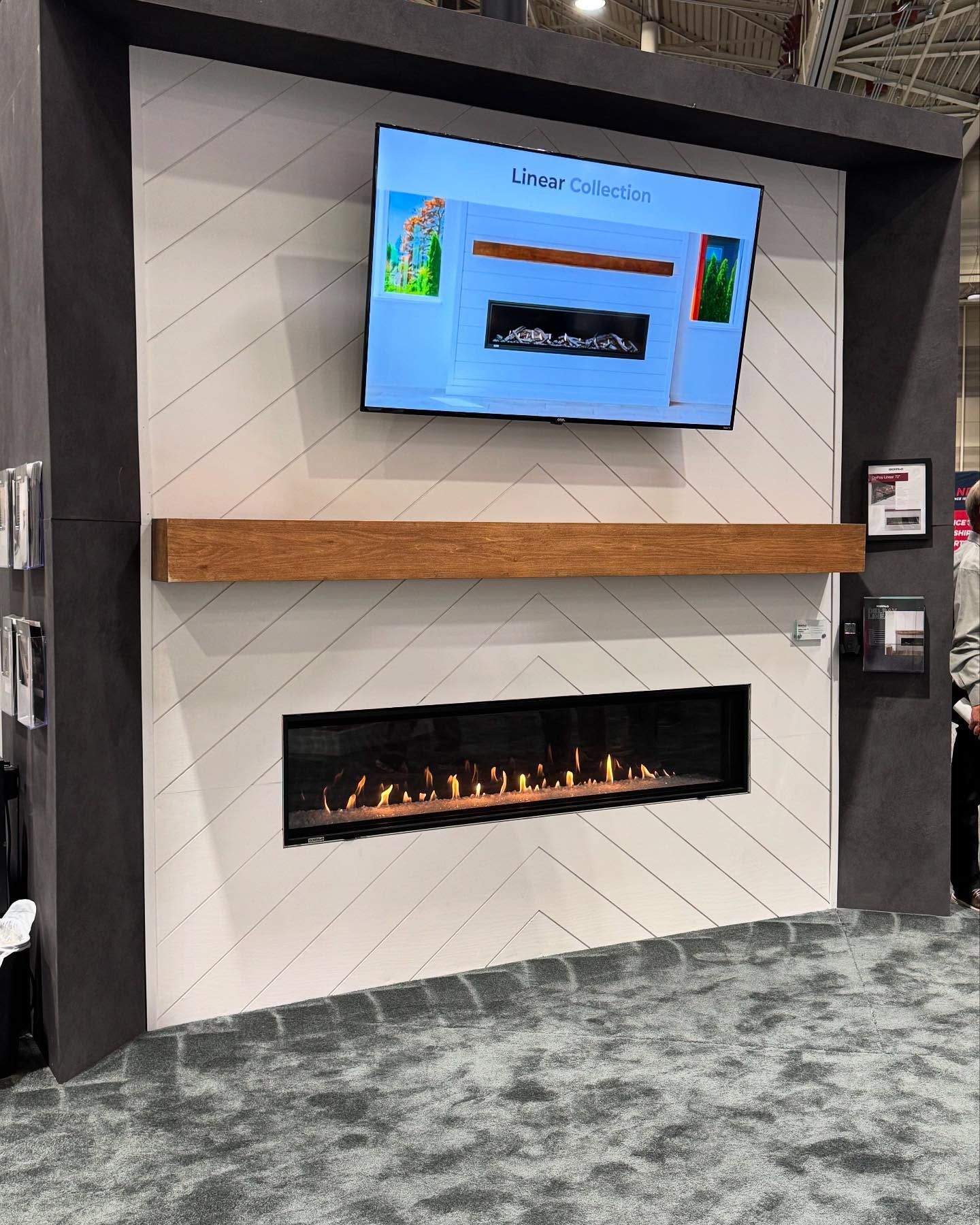 Fireplace display with a TV, wood mantel, and patterned white and gray wall.