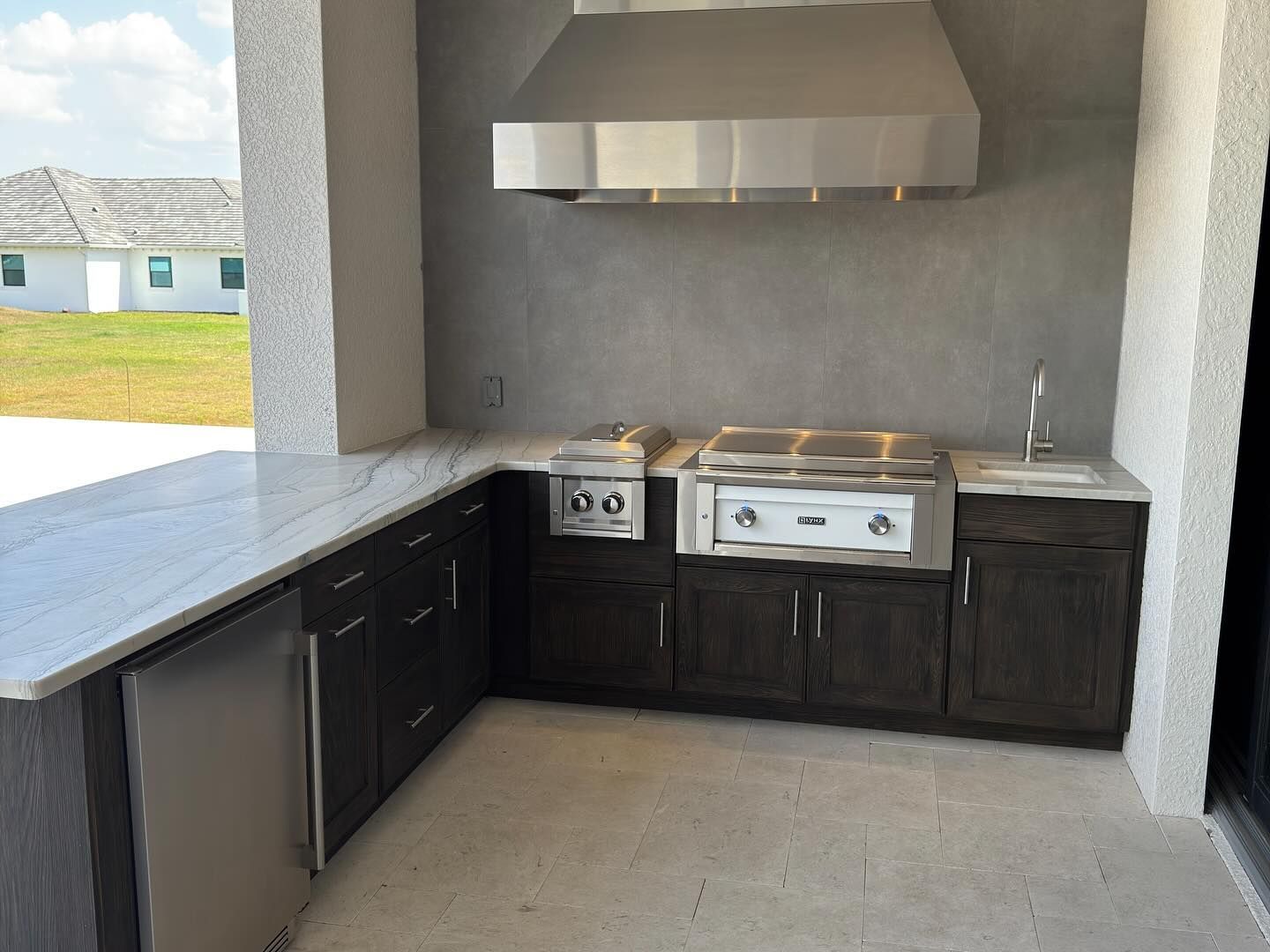 Outdoor kitchen with stainless steel appliances, dark cabinets, and gray countertop.