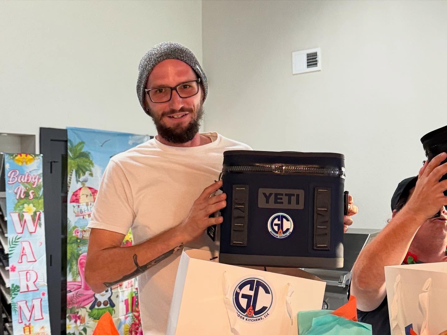 Man in beanie smiles, holding a dark blue YETI cooler with 