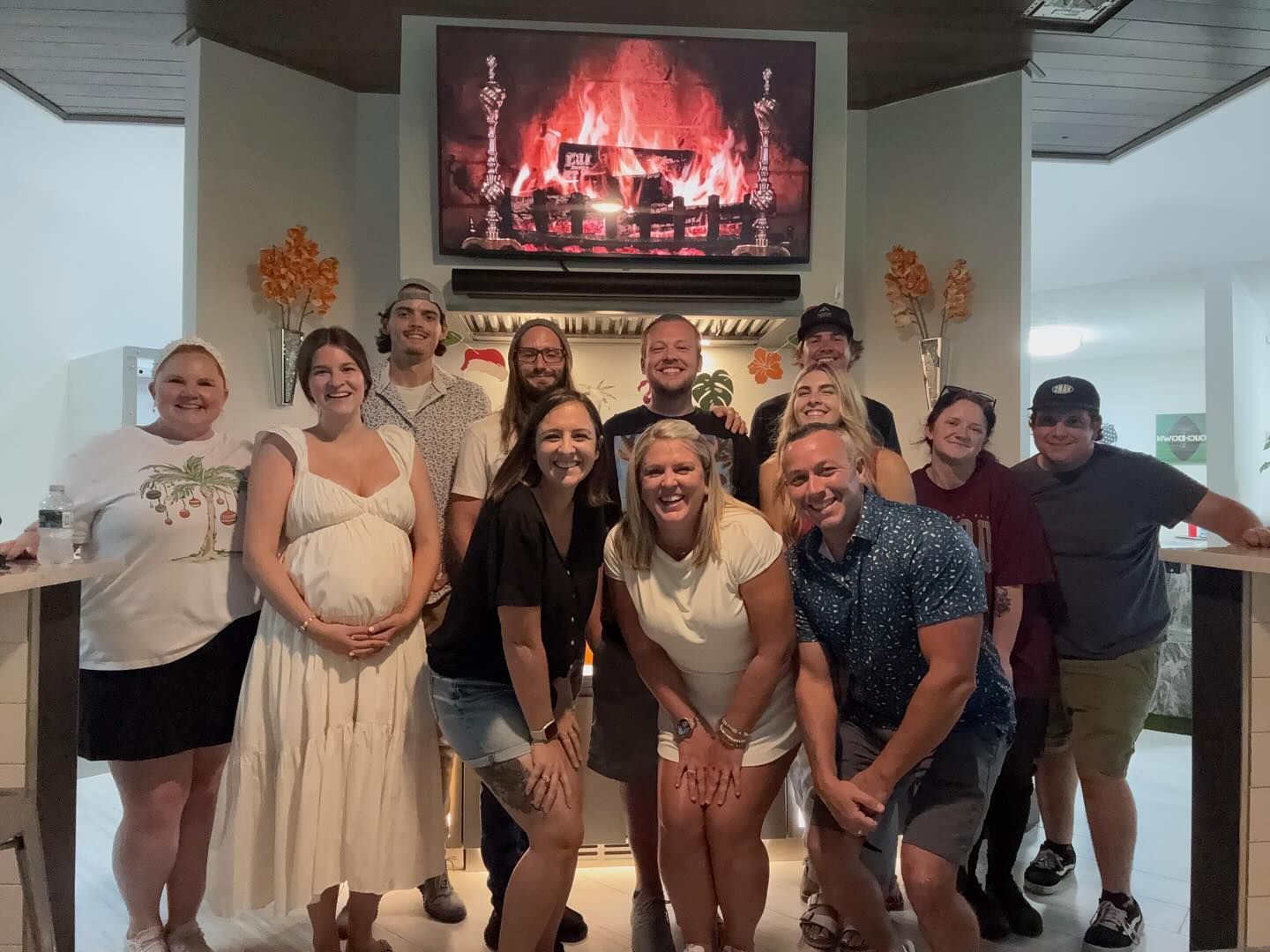 Group of people smiling together in front of a fireplace with a TV screen above.