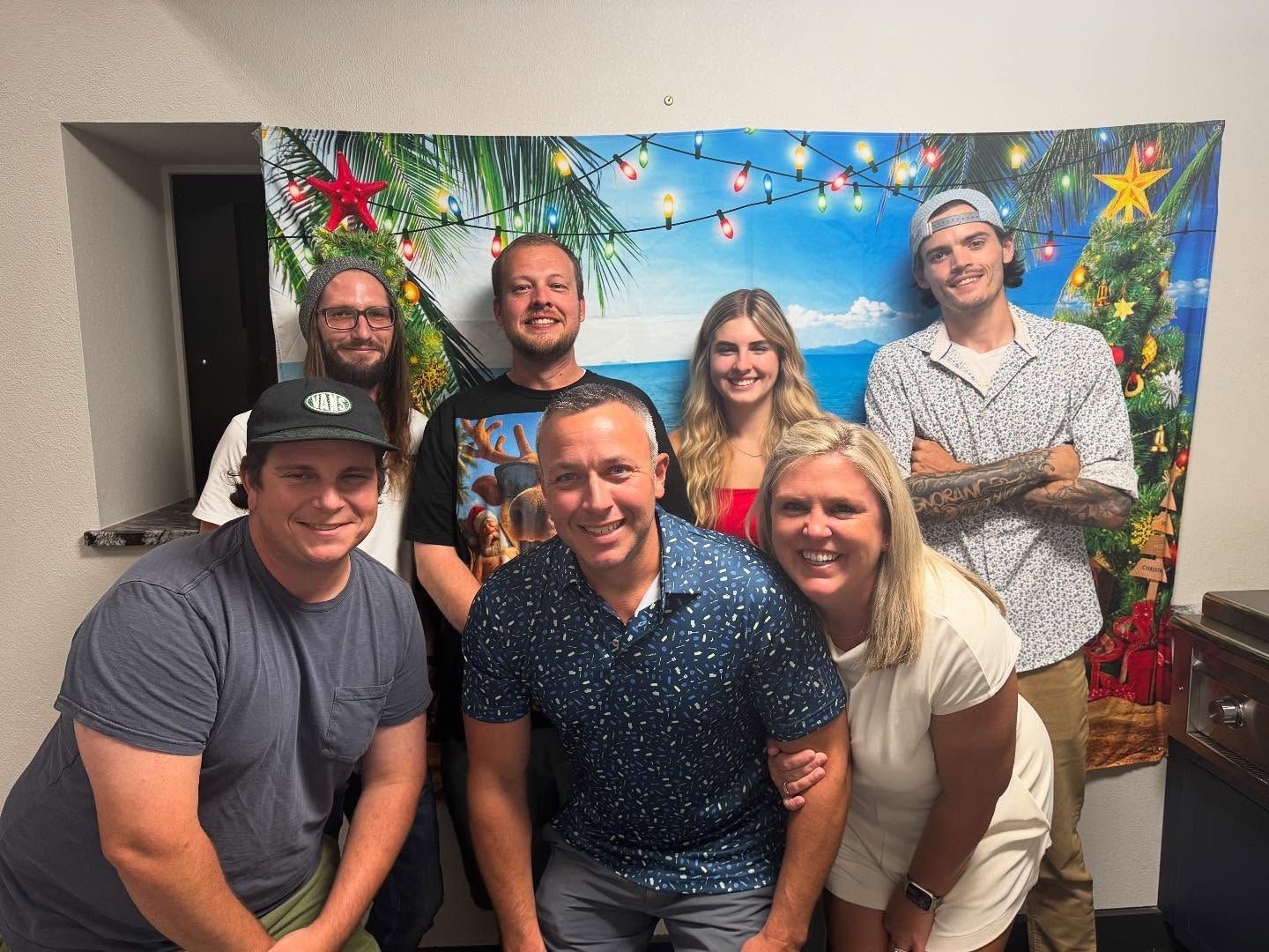 Group of people posing in front of a tropical-themed backdrop. They smile at the camera.