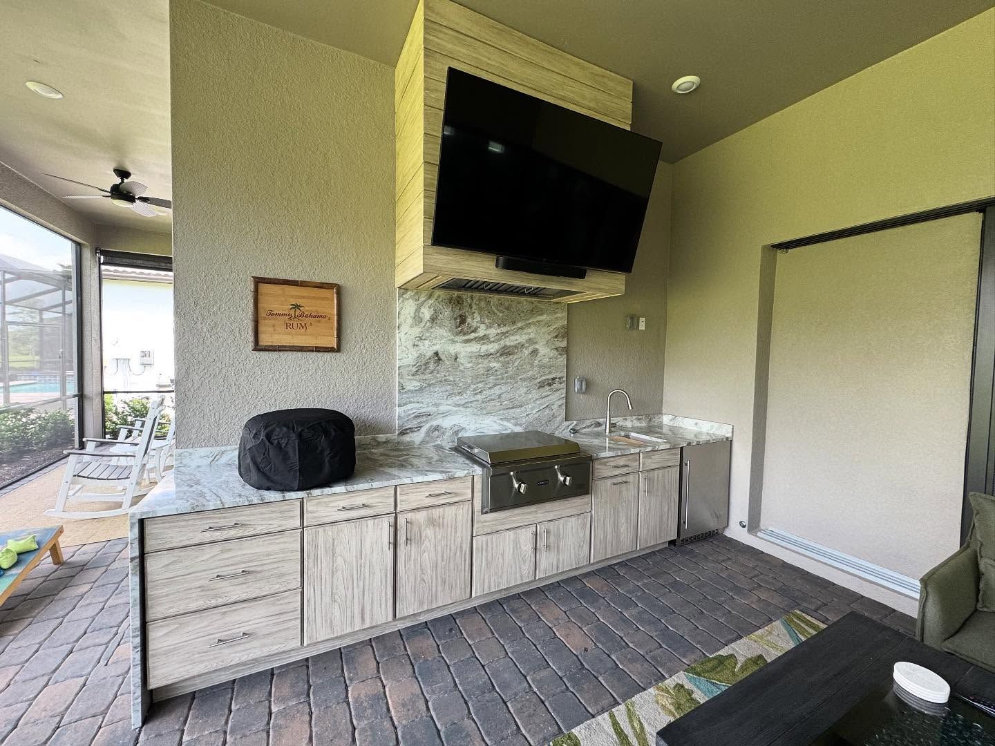 Outdoor kitchen with a TV, grill, and cabinets under a beige ceiling.