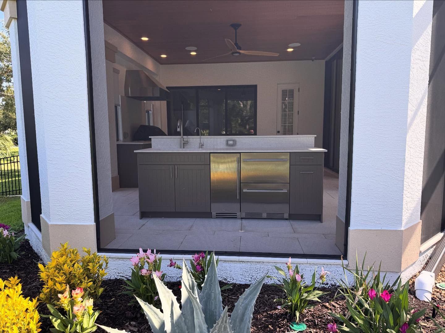 Outdoor kitchen with gray cabinets, stainless steel appliances, and a bar area.