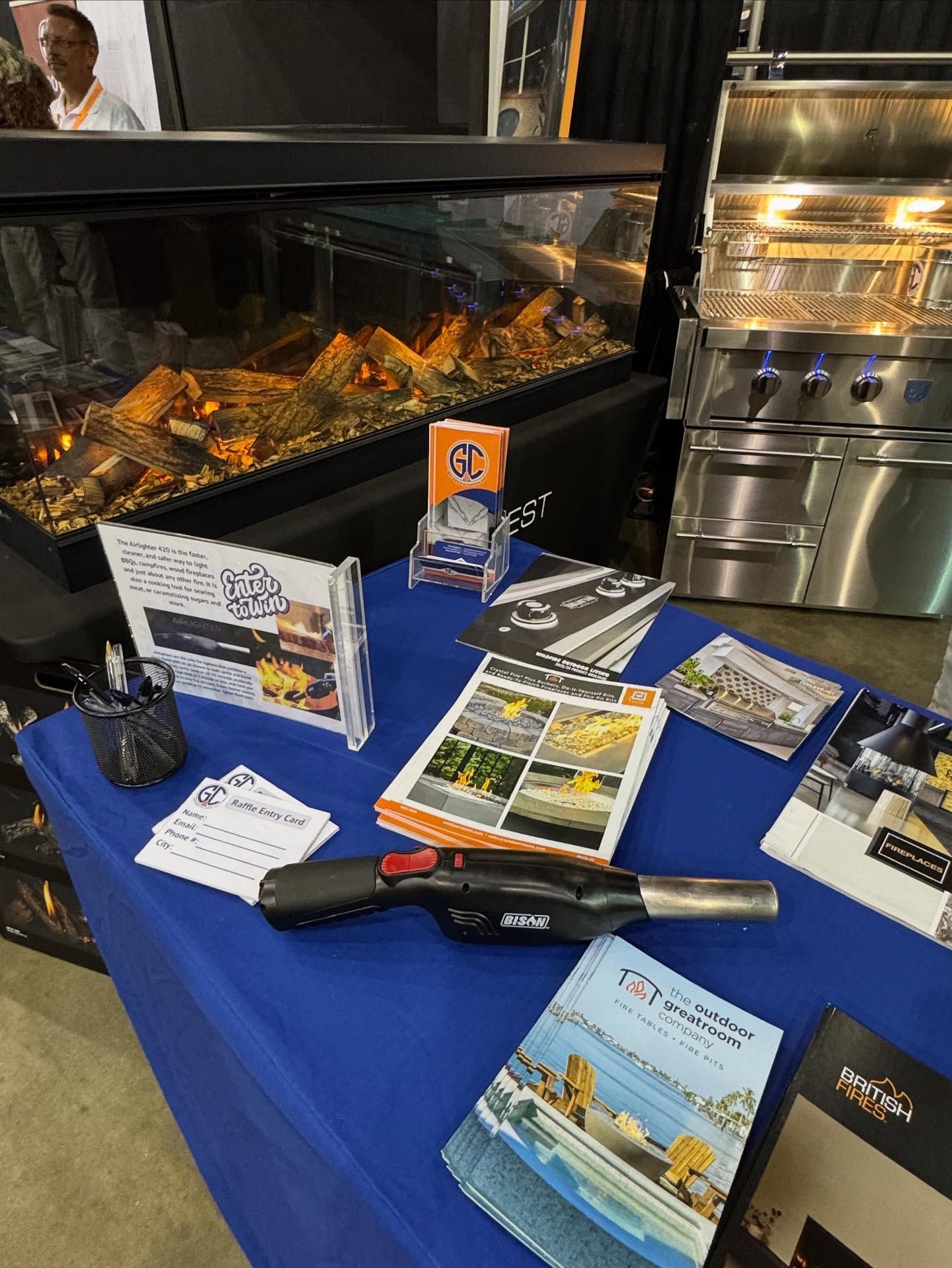 A trade show booth with brochures, a torch, and a display with an electric fireplace and built-in grill.
