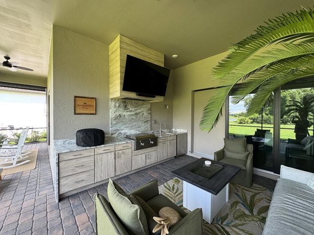Outdoor kitchen with stainless steel appliances, blue patterned tile backsplash, and dark cabinets.