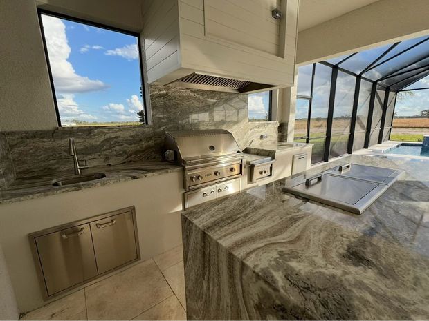 Outdoor grilling station with two stainless steel grills and gray cabinets on a patio, with an ocean view.