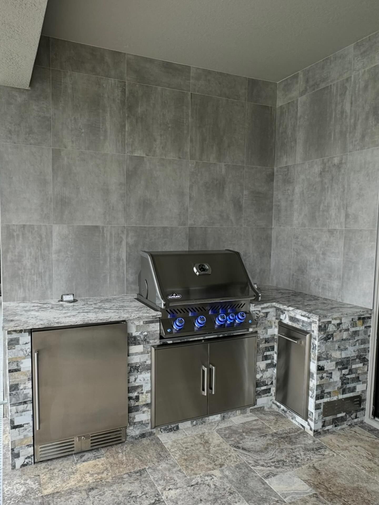 Outdoor kitchen with stainless steel grill, refrigerator, and tile backsplash.