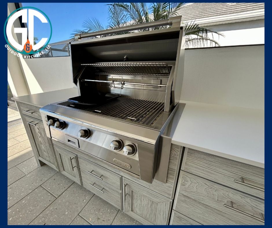 Outdoor kitchen with a stainless steel grill and gray cabinets, set on a patio.