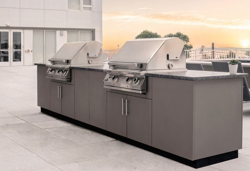 Two stainless steel grills built into a gray outdoor kitchen, on a patio at sunset.