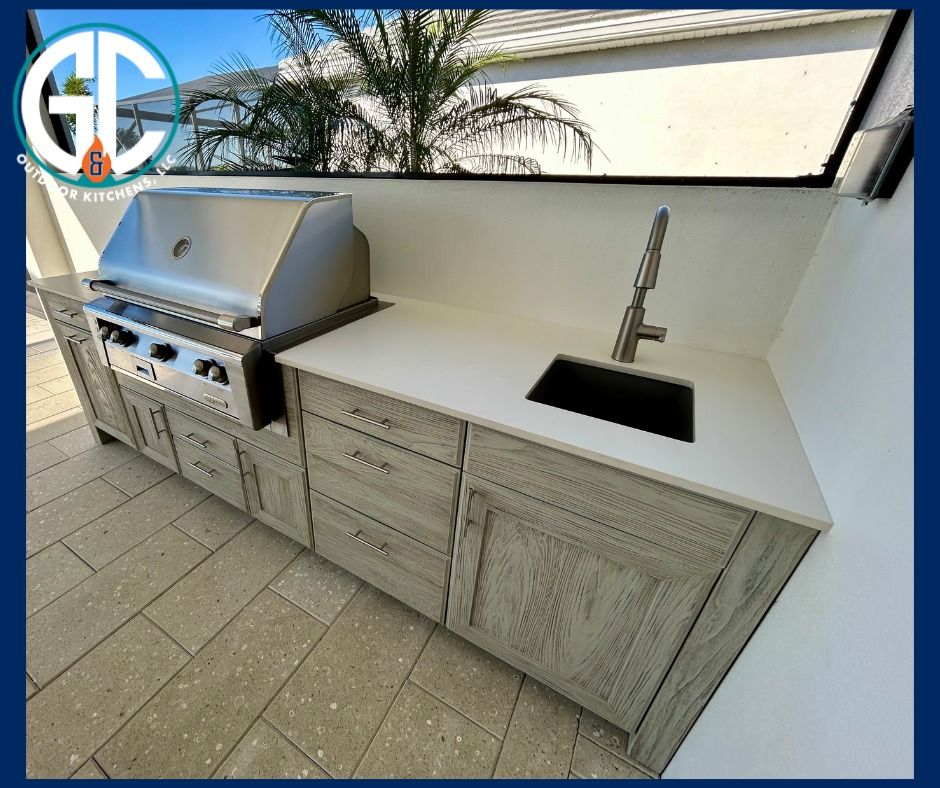Outdoor kitchen with a stainless steel grill, sink, and cabinets on a patio.
