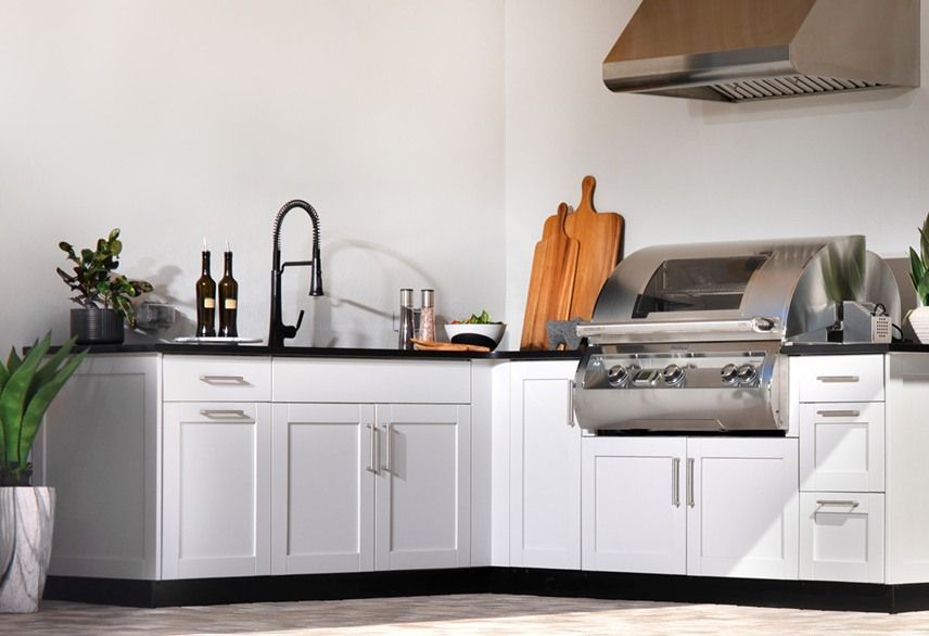 Outdoor kitchen with white cabinets, black countertop, stainless steel grill, sink, and hood.