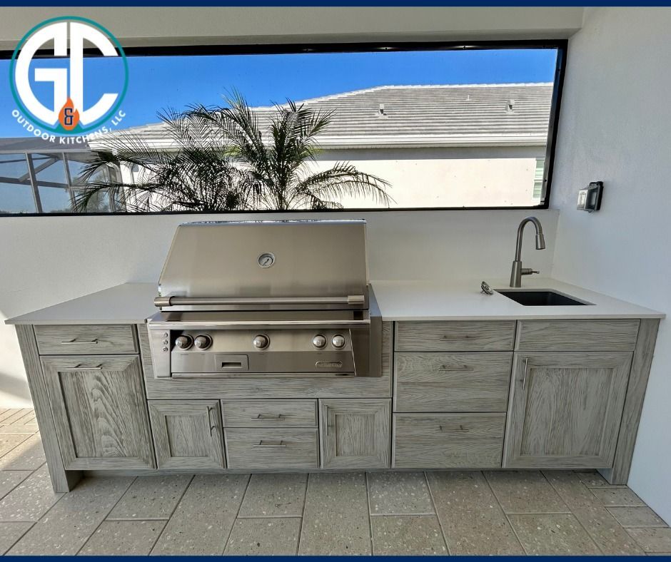 Outdoor kitchen with grill, sink, and cabinets under a window.