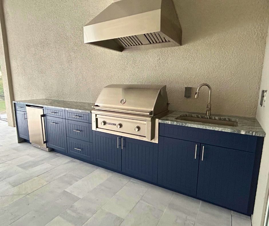 Outdoor kitchen with stainless steel grill, navy blue cabinets, and stone countertop.