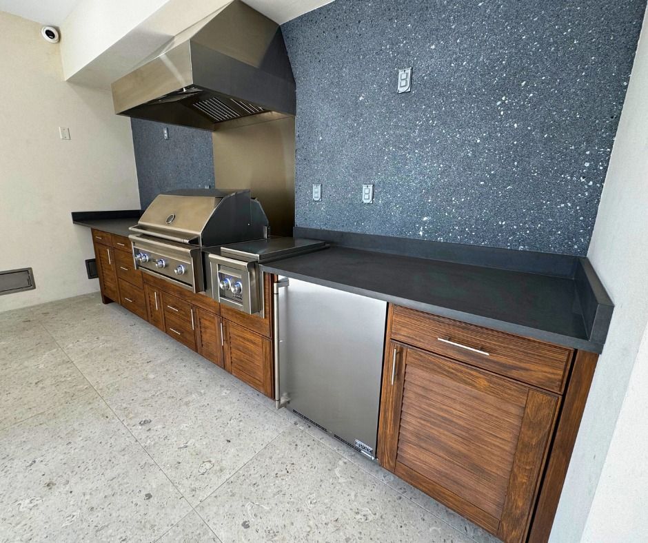 Outdoor kitchen with stainless steel grill, cabinets, dark countertops, and speckled gray wall.