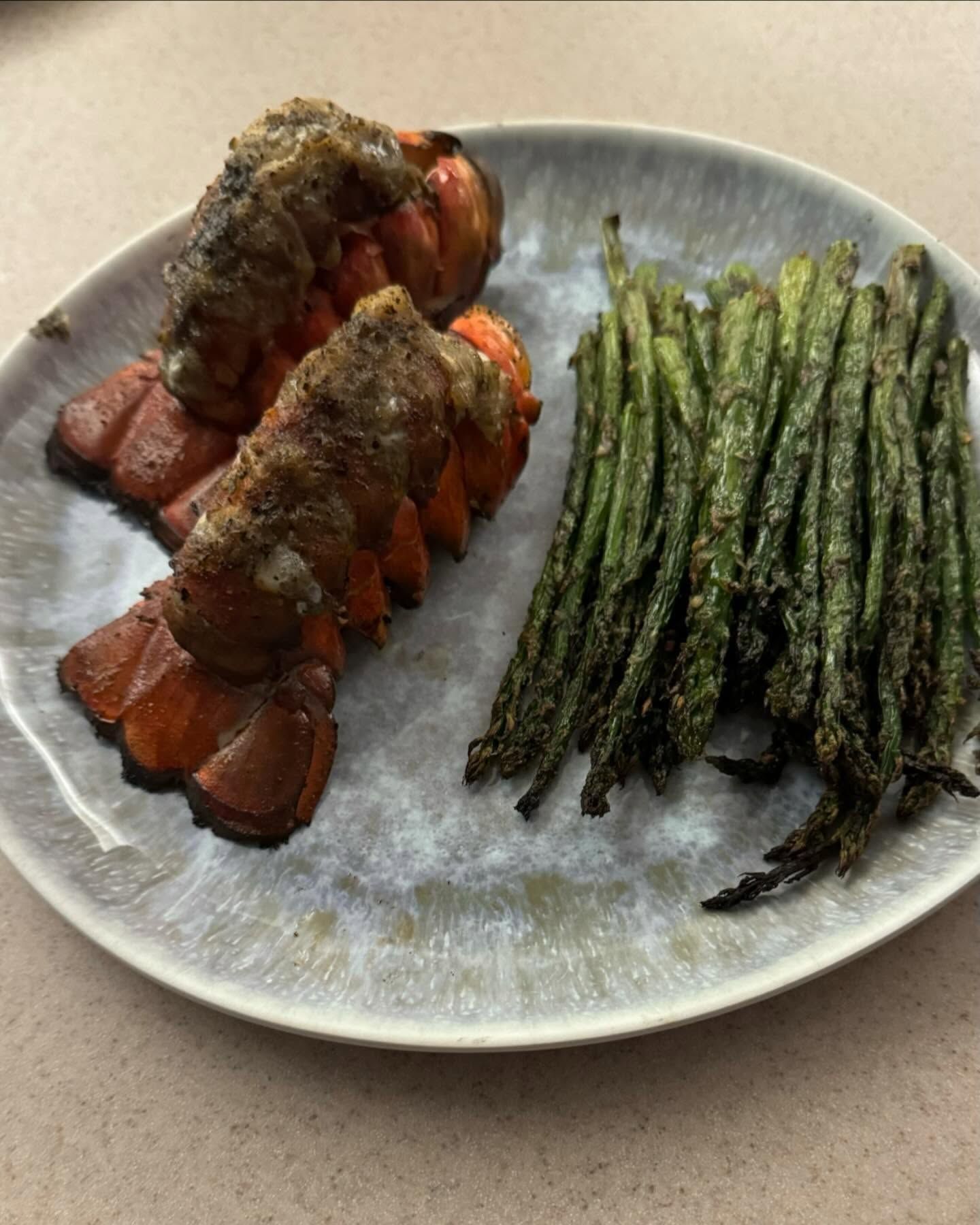 Lobster tails and roasted asparagus on a speckled gray plate.