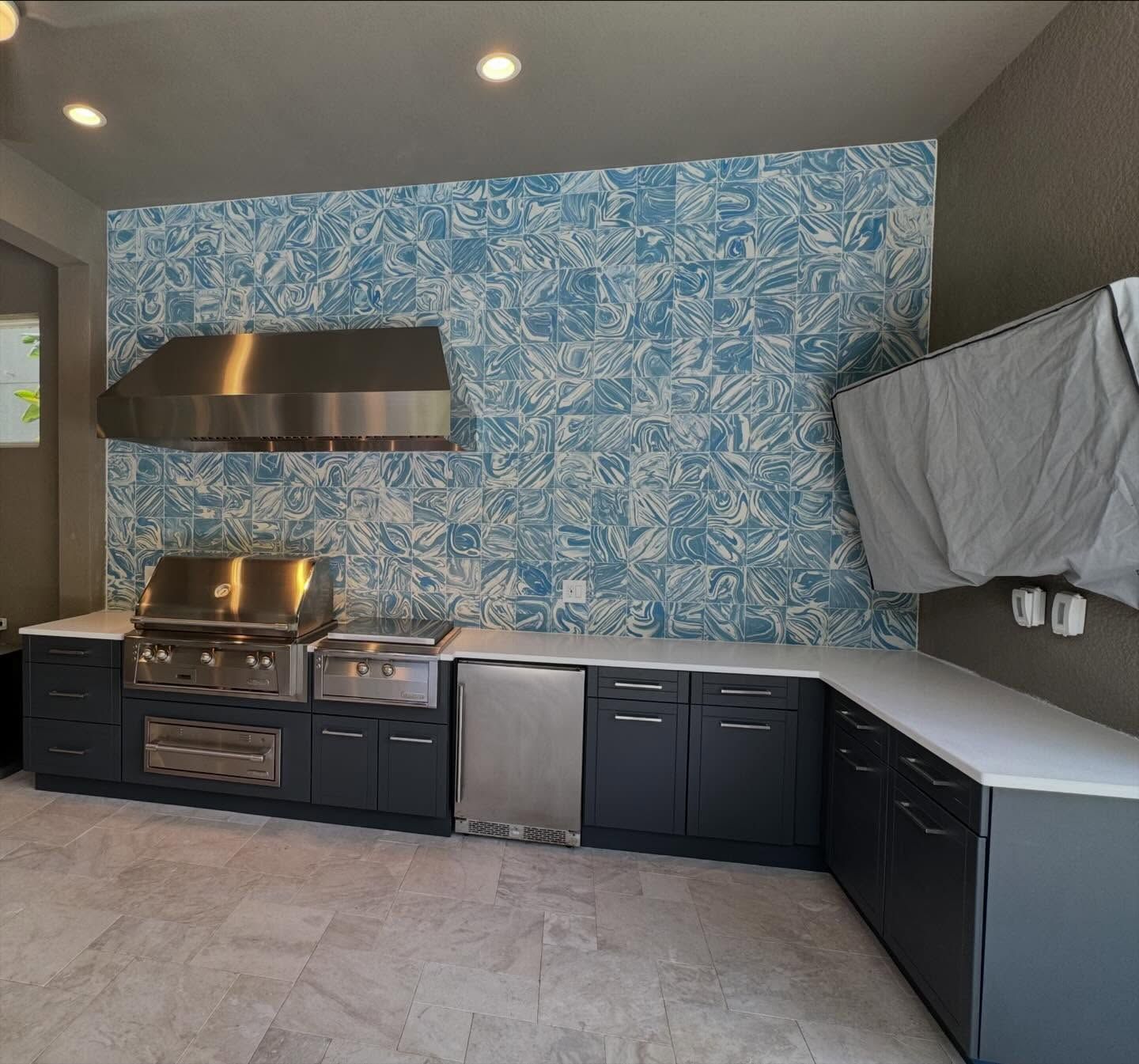 Outdoor kitchen with stainless steel appliances, blue tile backsplash, and gray cabinets.