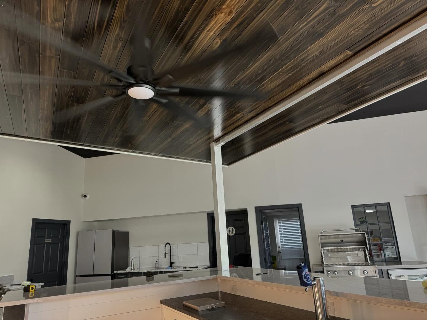Outdoor kitchen with wooden ceiling, ceiling fan, and stainless steel appliances.