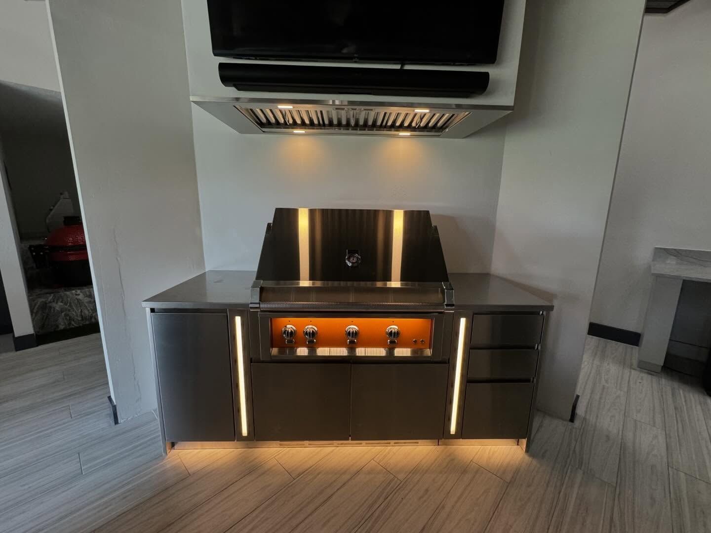 Outdoor kitchen with a stainless steel grill, cabinets, and a mounted TV.