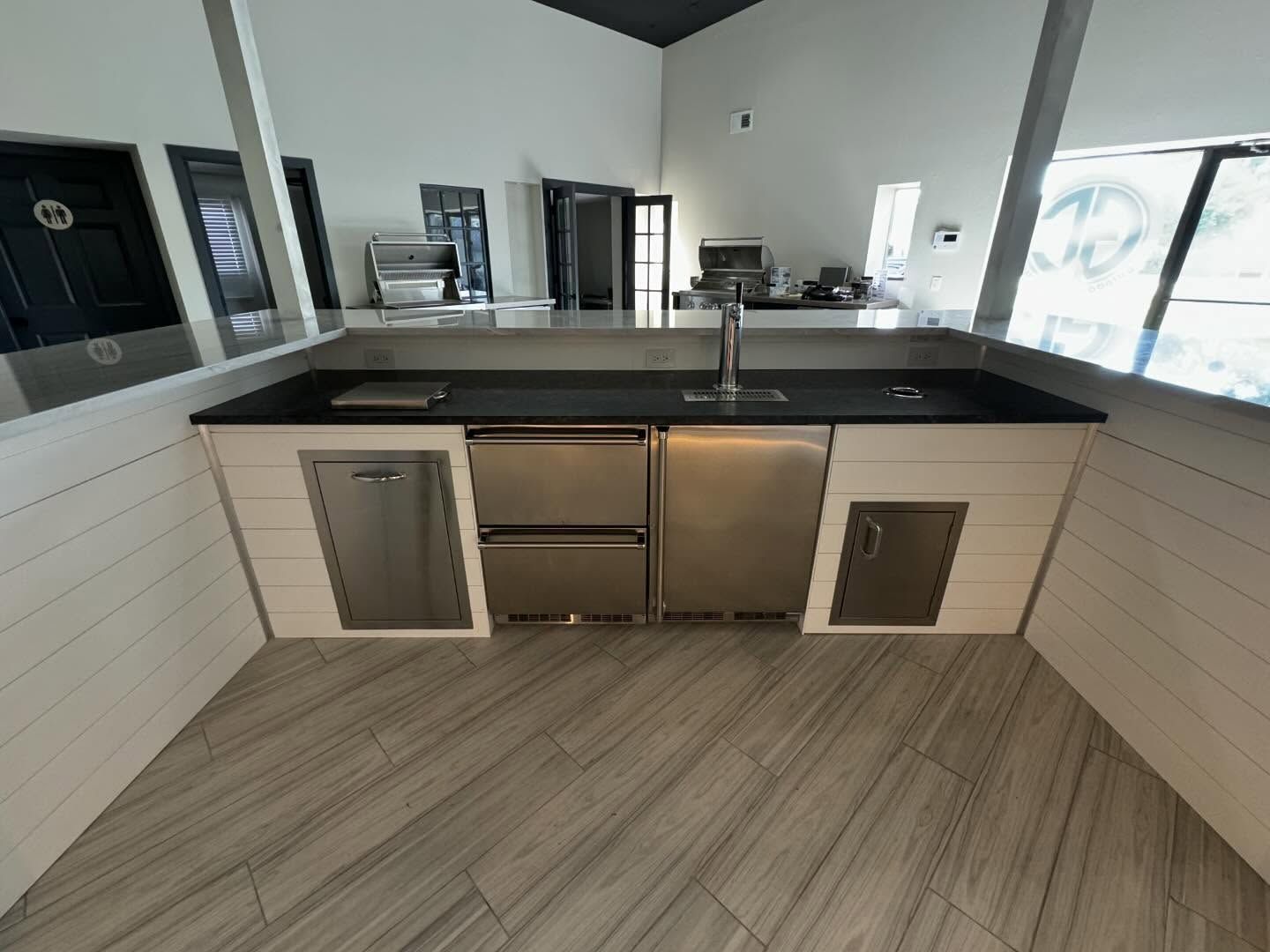 Outdoor kitchen with a black countertop, stainless steel appliances, and white cabinets.