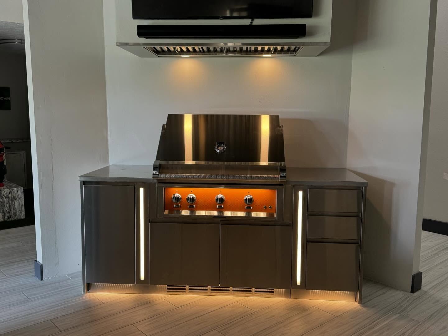 Outdoor kitchen with grill, cabinetry, and overhead lighting.