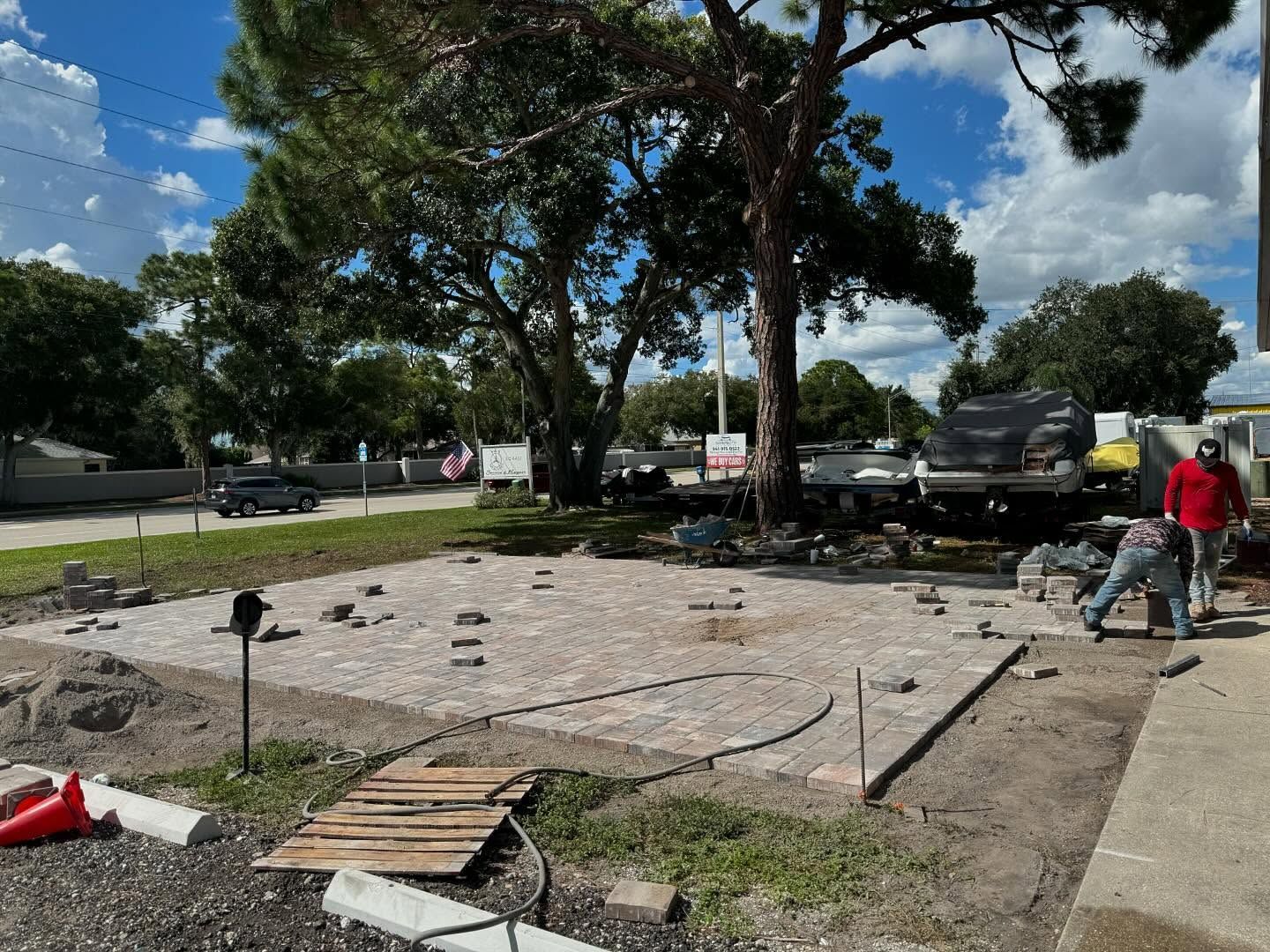 Construction site: men laying bricks. Tree in background, truck, and blue sky.