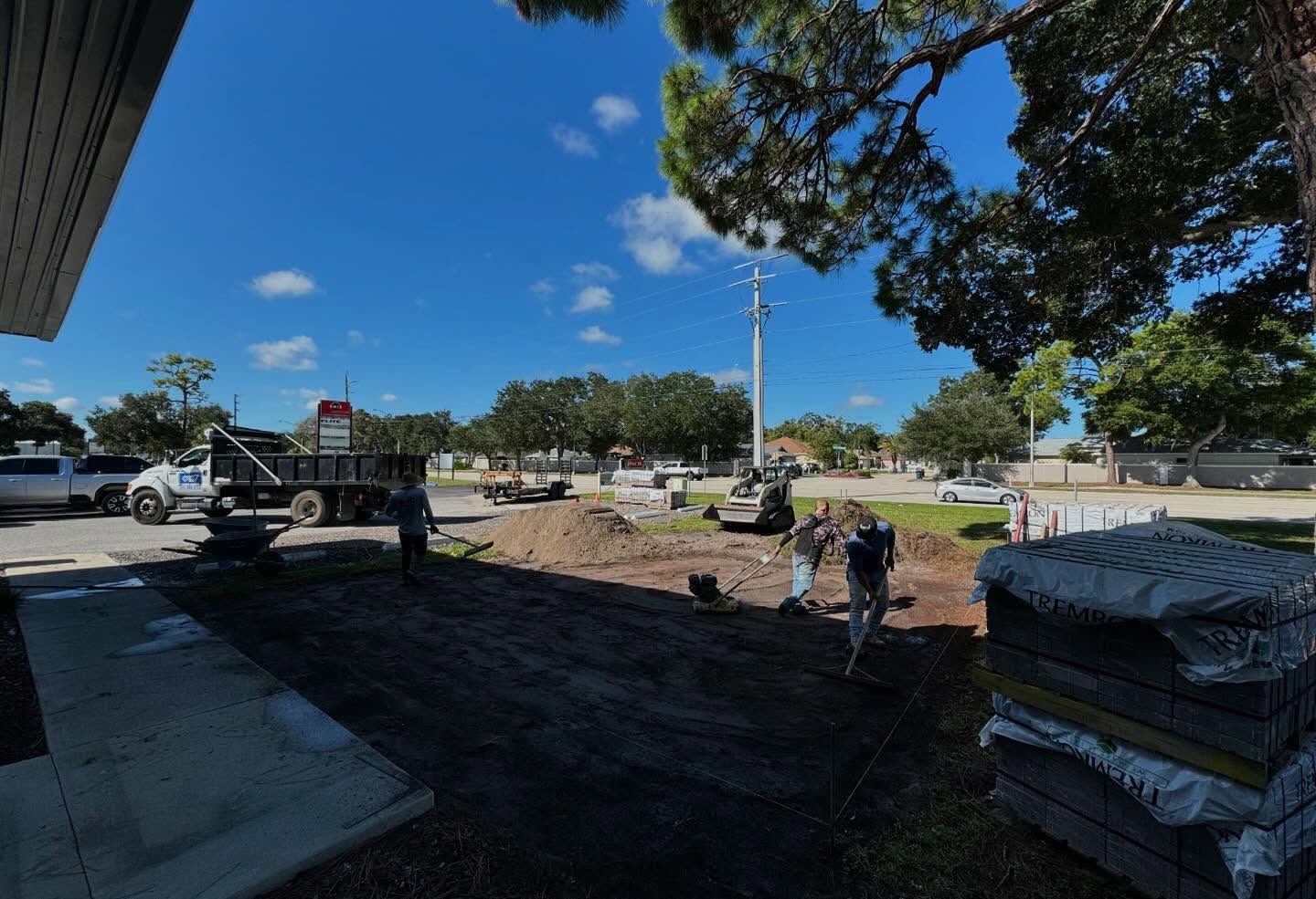 Construction site with workers, truck, and equipment under a blue sky, preparing ground.
