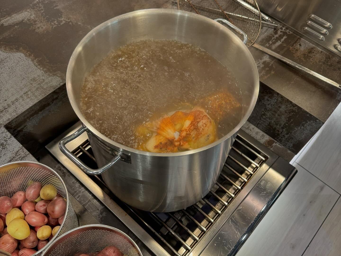 Pot of boiling water with lobster cooking on a stovetop, red potatoes in foreground.