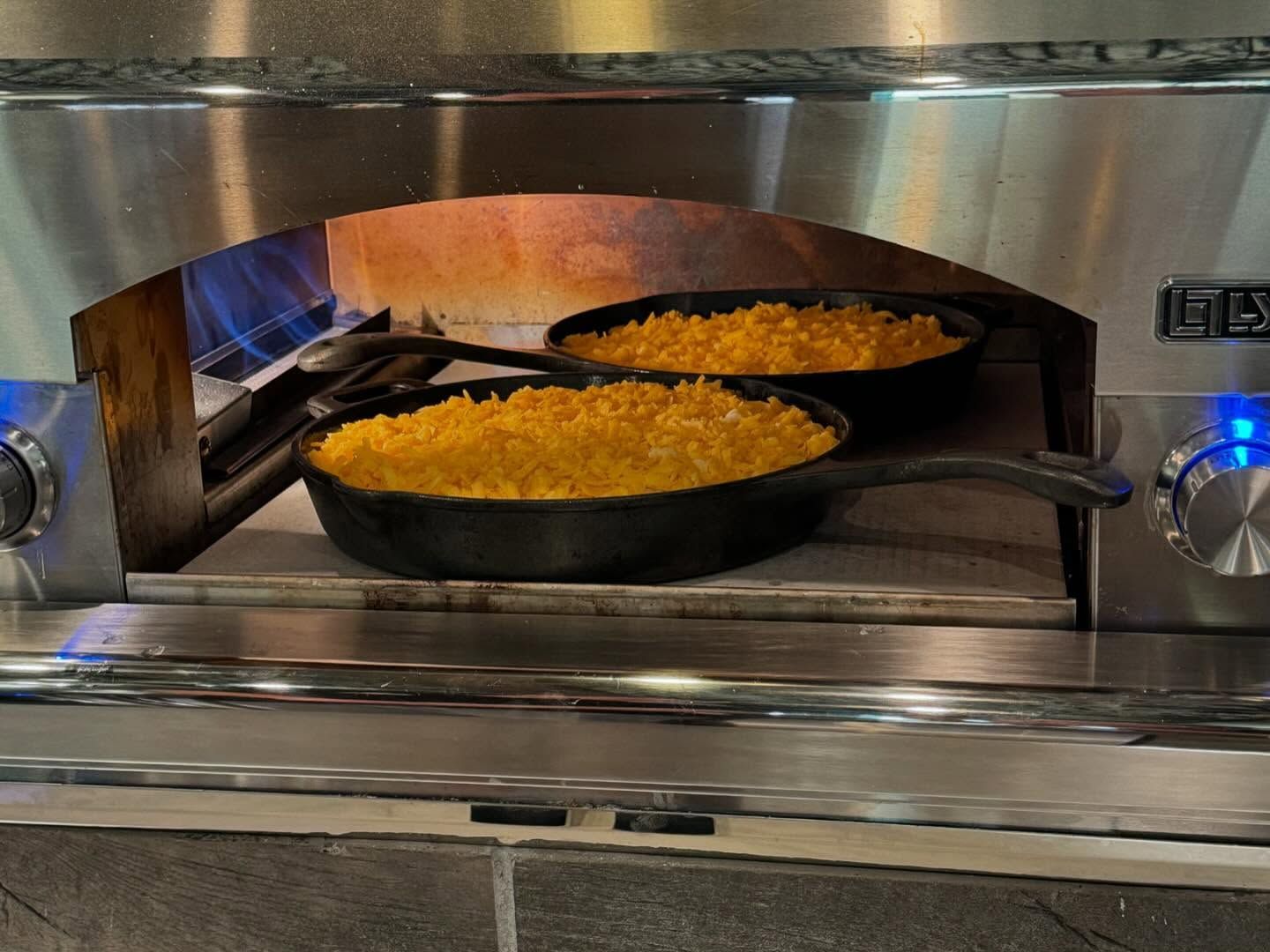 Two cast iron skillets with golden-crusted food baking inside a stainless steel oven.
