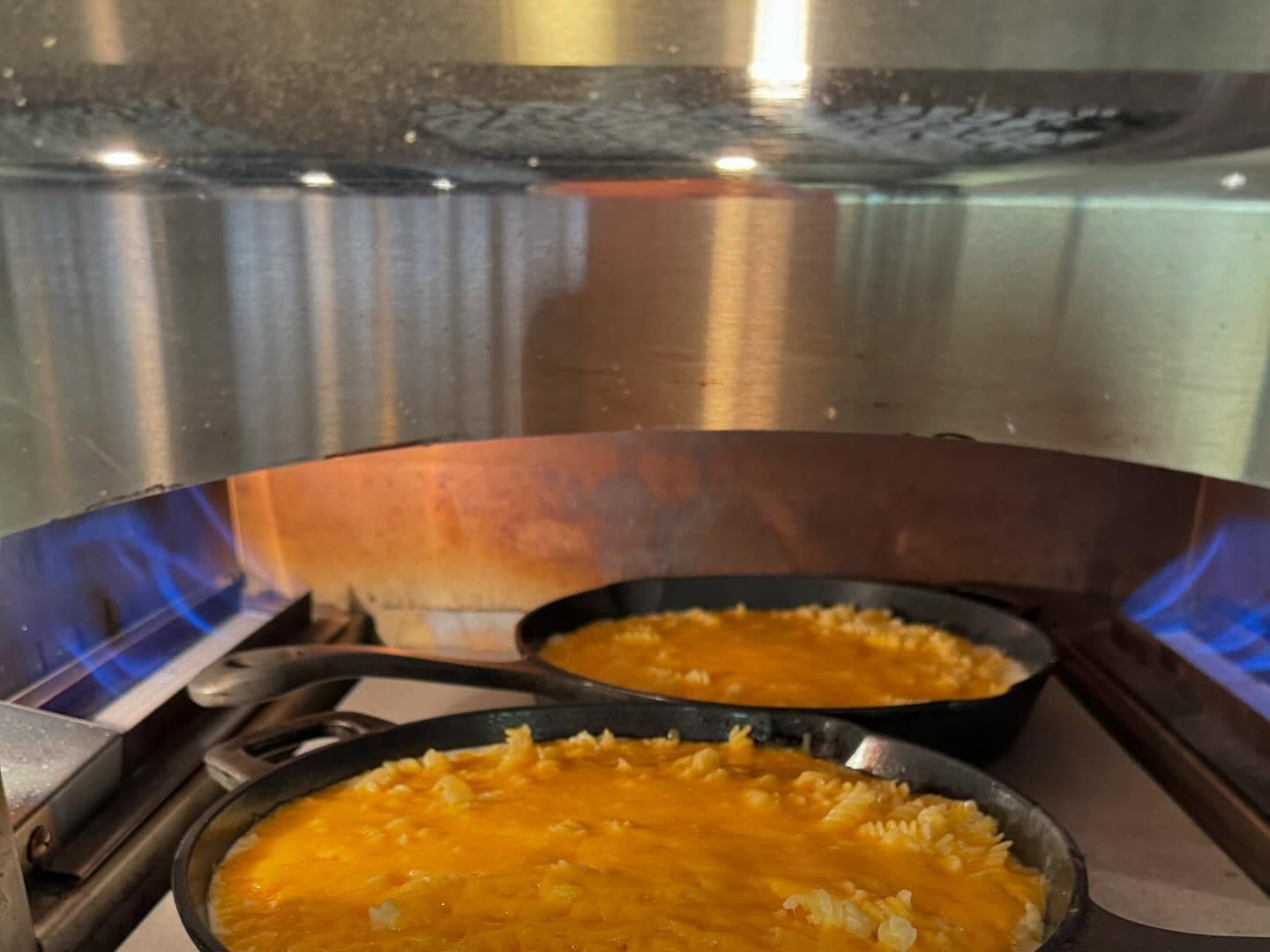 Two cast iron skillets with golden-brown food cooking over gas flames inside an oven.