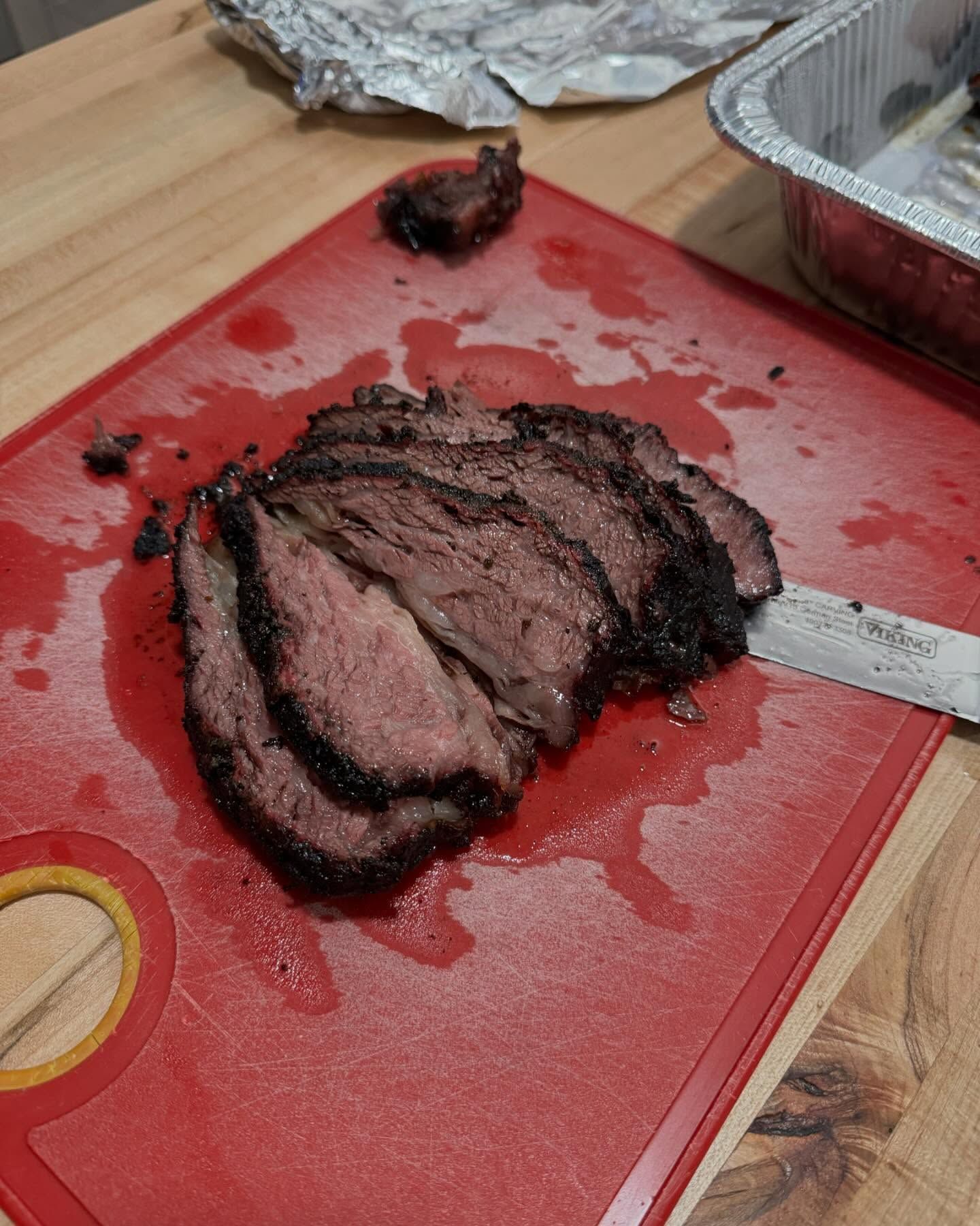 Sliced brisket on a red cutting board, knife to the side. Smoky bark, pink interior.