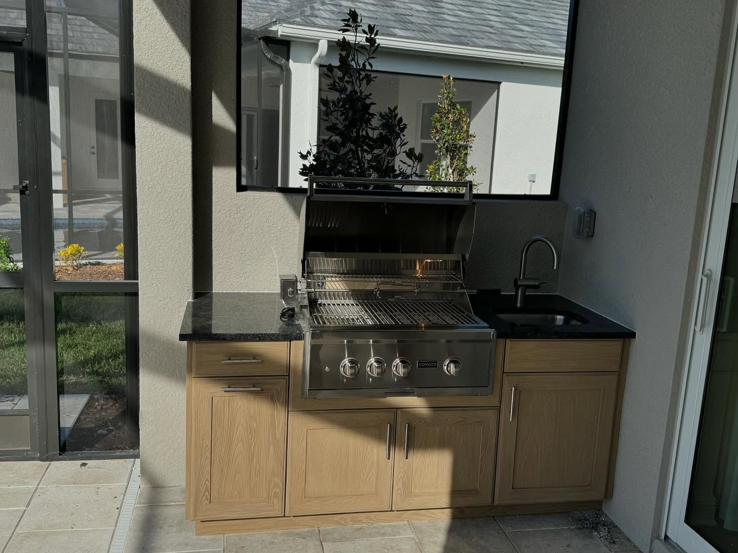 Outdoor kitchen with grill, sink, and cabinets under a TV screen.