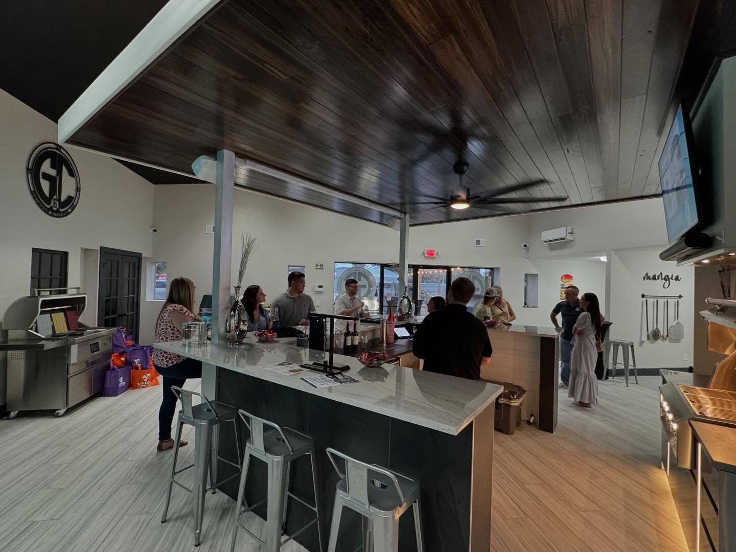 Interior of a kitchen/bar area with people socializing. Modern design with wooden ceiling, and a large countertop.