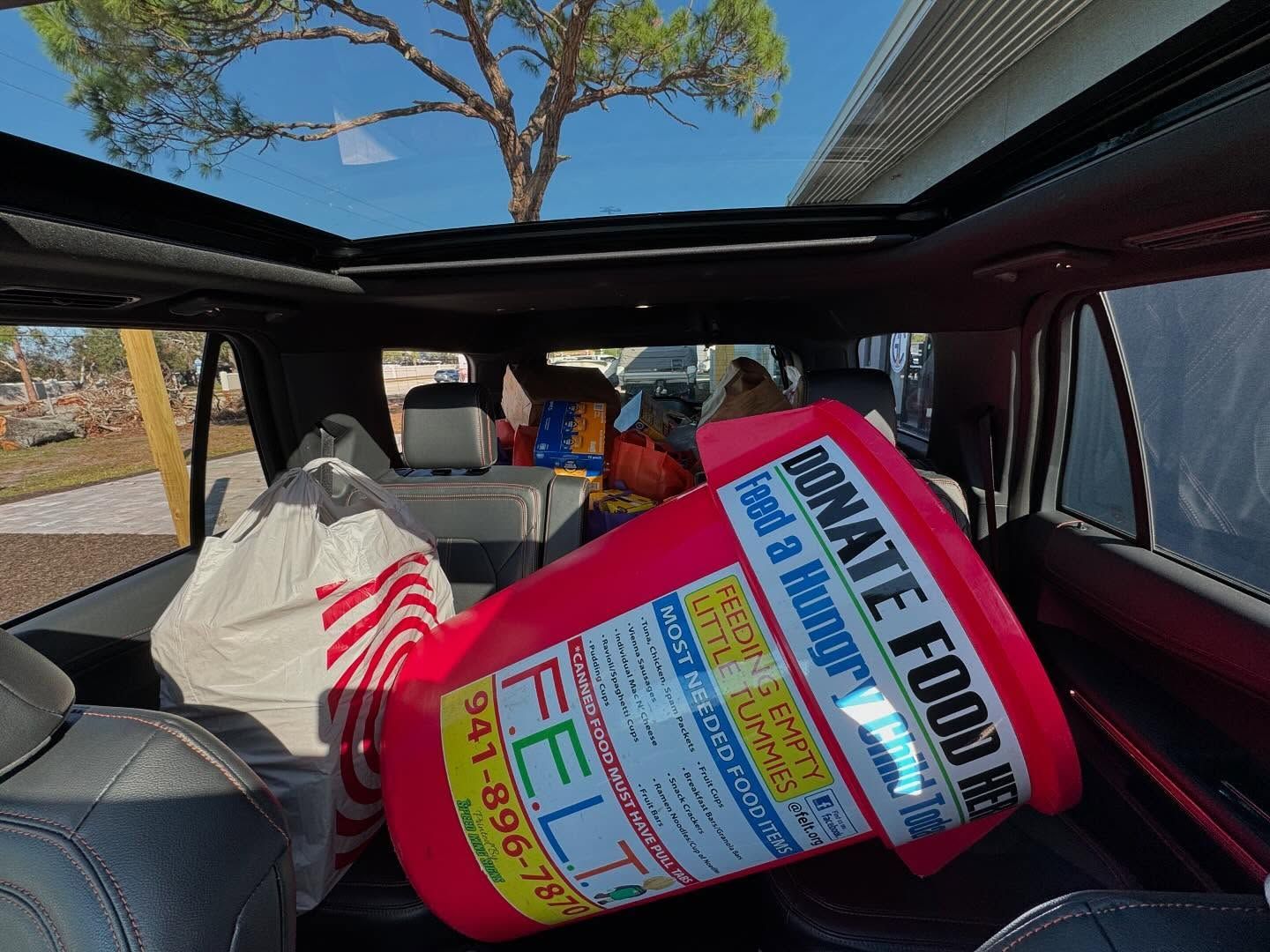 Back of a car filled with donation items, including a large red container that reads 