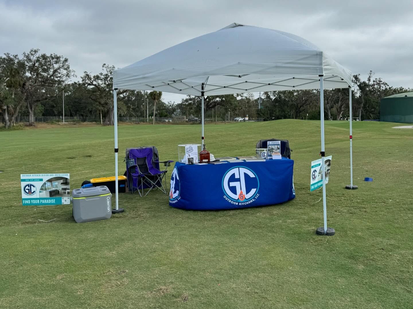 A white canopy on a grassy golf course with a table and logo for 