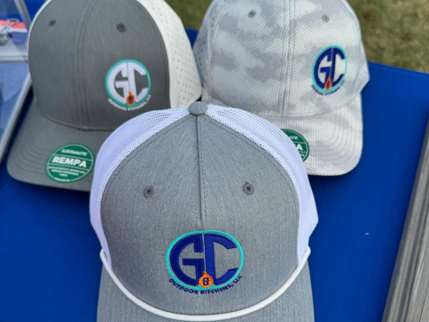 Three gray and white GC logo caps on blue surface.