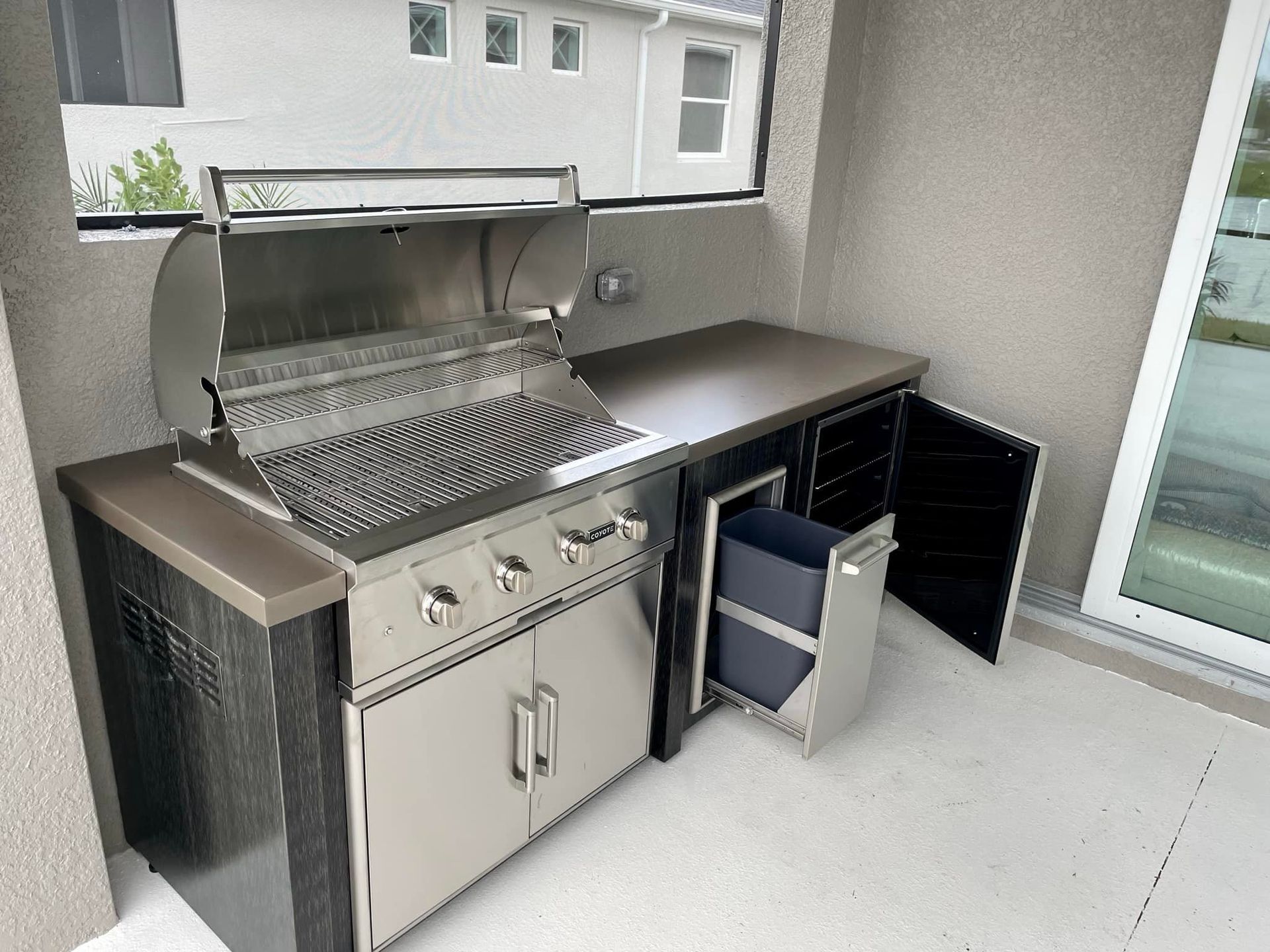 Outdoor kitchen with grill, countertop, cabinets, and a pull-out trash bin.