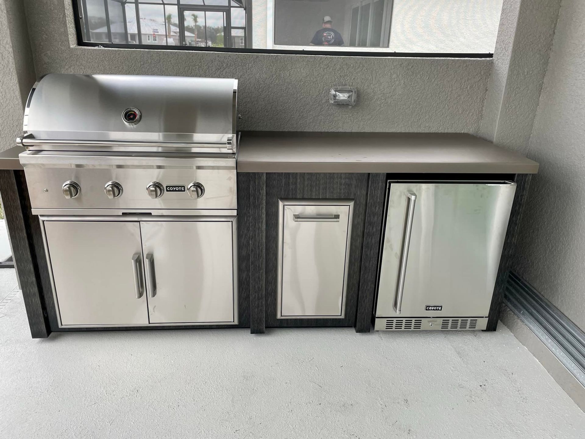 Outdoor kitchen with a stainless steel grill, cabinet, and refrigerator.