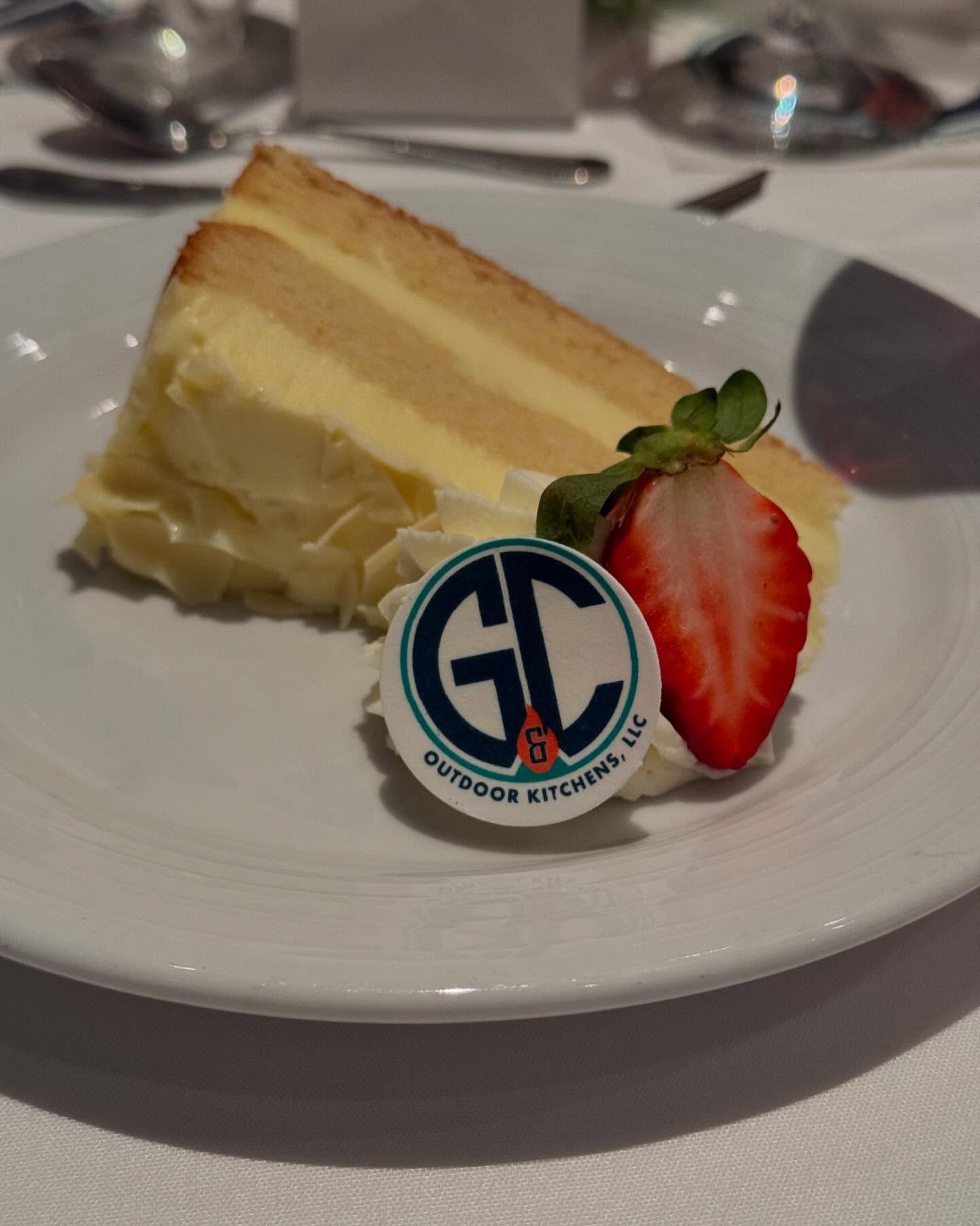 Slice of layered cake with white frosting, strawberry, and GC logo on plate.