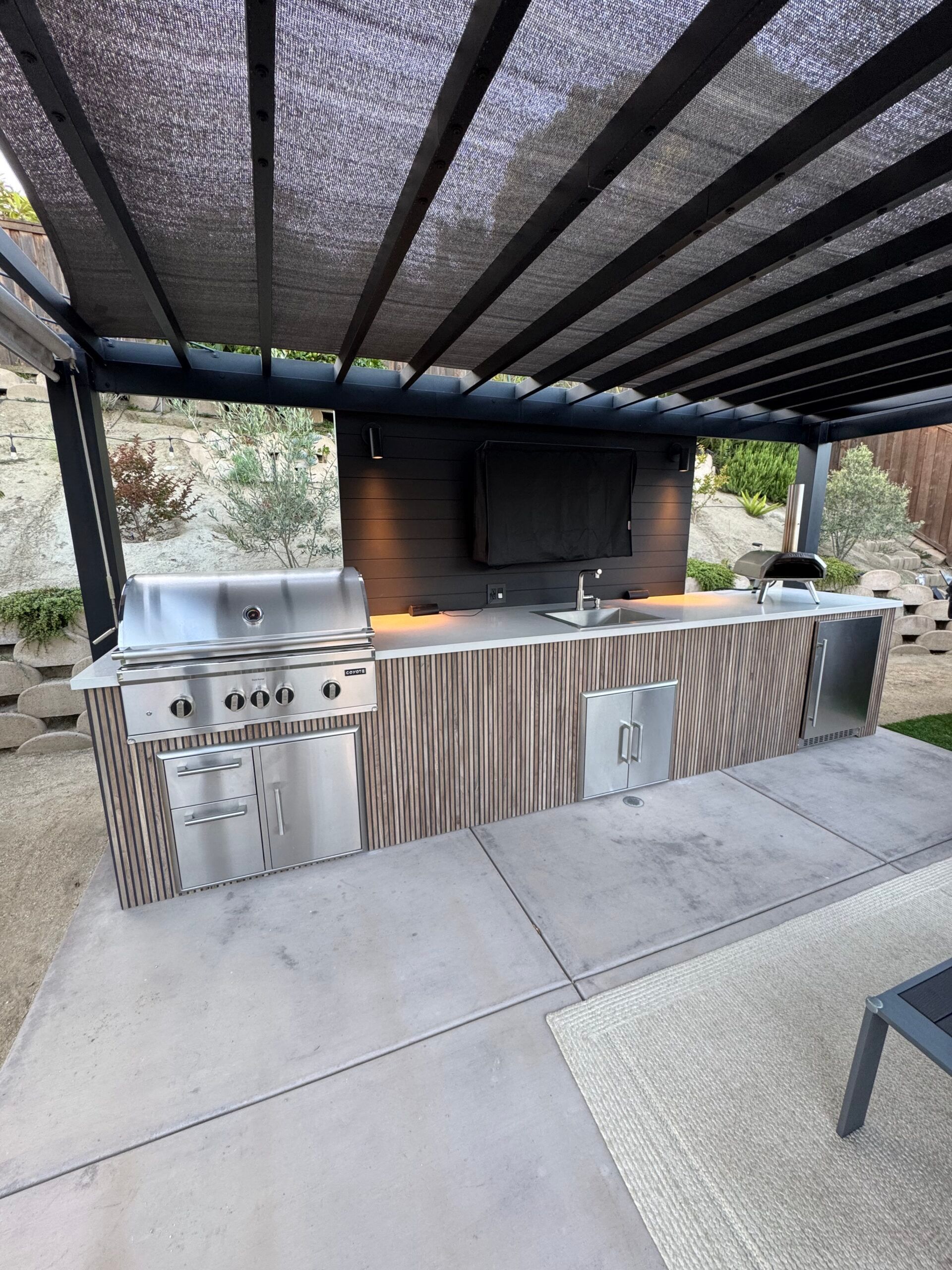 Outdoor built-in grill and countertop under a covered patio with striped shade canopy