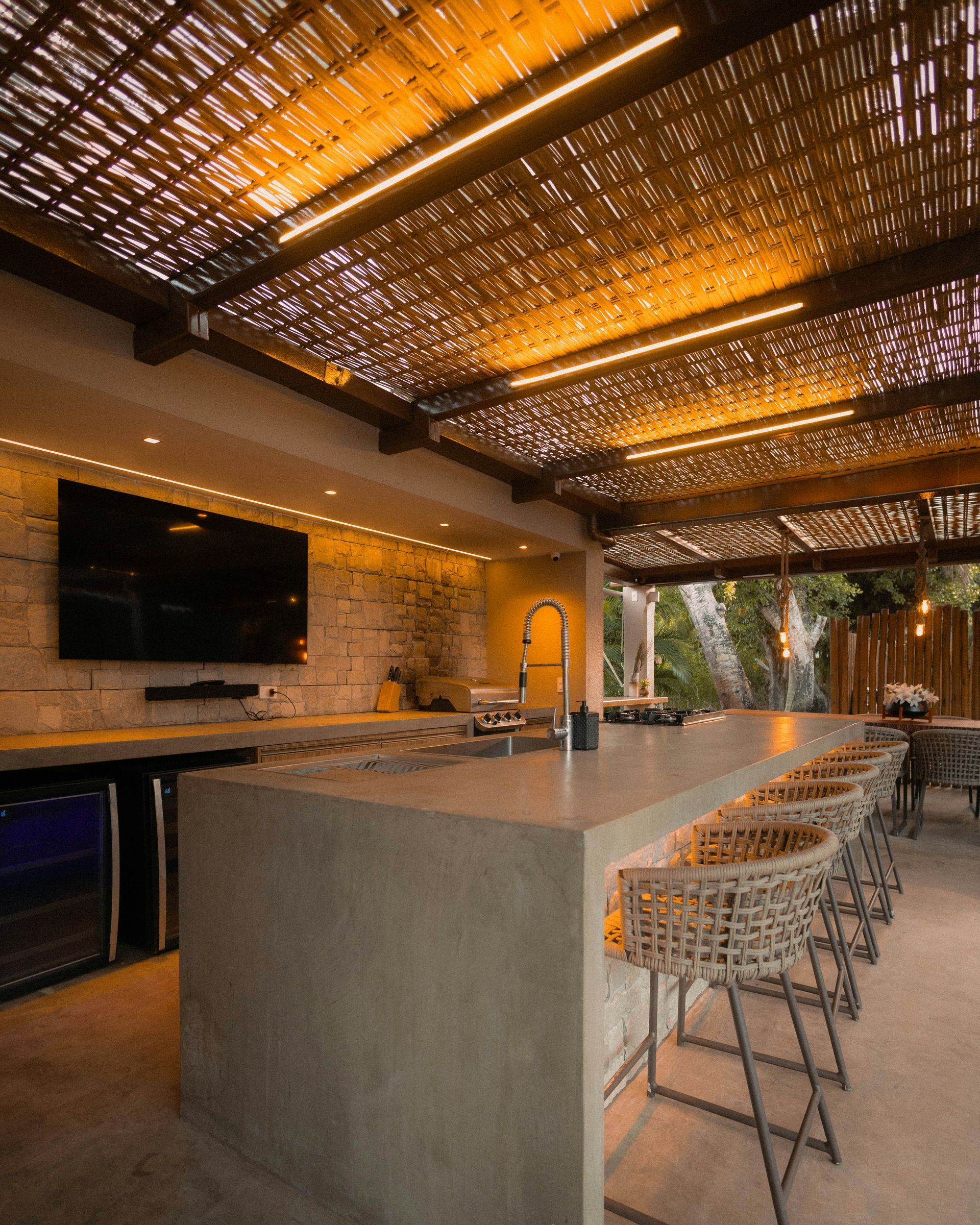 Outdoor bar with concrete counter, woven bar stools, and a bamboo ceiling. Includes a television and built-in cooler.